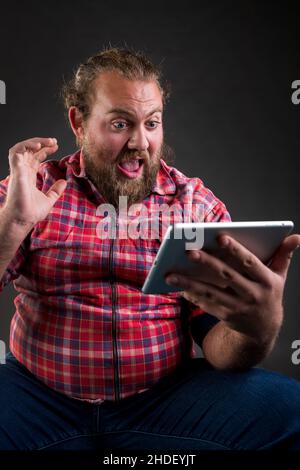 Portrait of a bearded man reading a shocking e-mail on digital tablet. Stock Photo