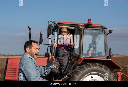 Senior man driving a tractor and arguing with a farm worker on organic farm. Stock Photo