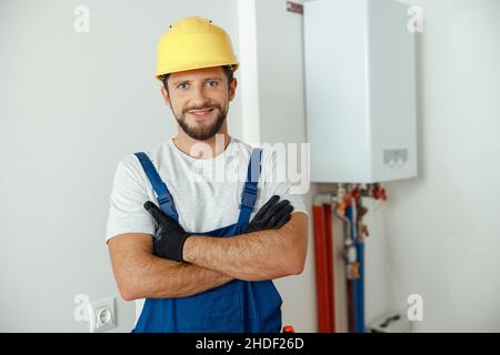 Cheerful male worker, technician servicing the house heating system smiling at camera while standing with arms crossed Stock Photo