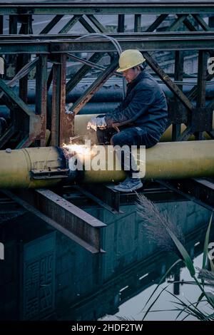 Vertical shot of a construction worker sitting and working on a pipe Stock Photo