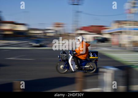 Closeup of man in an orange jacket and a white helmet riding a motorcycle Stock Photo