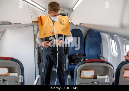 Flight attendant demonstrating how to use life vest in airplane Stock Photo