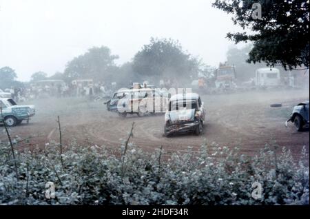 Banger racing featuring beat up painted cars racing around causing a dusty and smoky atmosphere. 1970s Stock Photo