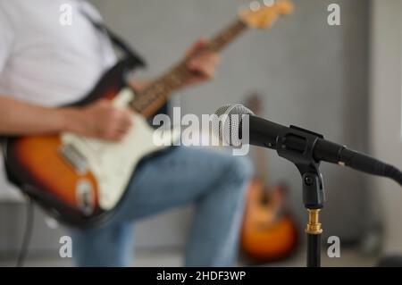 Microphone in recording studio or rehearsal room on background of musician on blurred background. Stock Photo