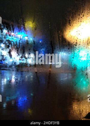 Bright colored lights through misted glass. Rain. Drops on glass. Urban evening backgrounds. Stock Photo