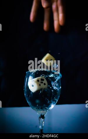 Vertical shot of a hand throwing two dices t a full of water wine glass Stock Photo
