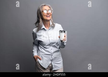 Morning coffee to go. Charming senior woman in formal wear standing with paper cup of hot drink isolated on gray, preparing to good working day. Mature business lady takes a coffee break Stock Photo