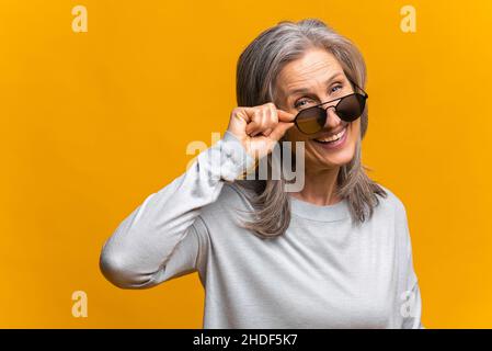 Photo of confident mature female model wears trendy sunglasses, prepares for date, isolated on yellow background, has fashion look Stock Photo