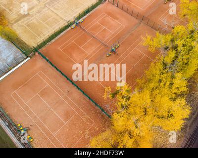 Look down on orange clay tennis courts in city park. Vivid yellow autumn trees near sports recreation area. Aerial treetop view on colorful Kharkiv, t Stock Photo