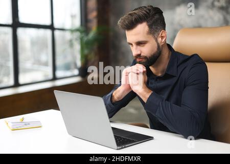 High angle view of the concentrated man looking at the laptop screen with serious expression while looking from the office. Serious guy at work Stock Photo