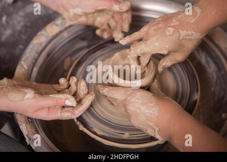Close up shot of two pairs of female hands working with clay on potters wheel Stock Photo