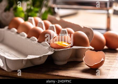 A cardboard box full of fresh chicken eggs with yolk in broken egg on the kitchen counter. Stock Photo