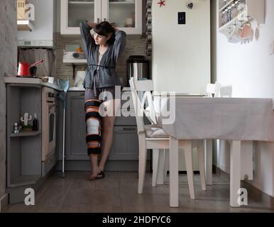 Young woman standing in the kitchen and looking out through the window. Stock Photo