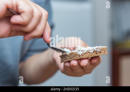 Woman preparing breakfast, putting soft cheese on rye bread. Female hands making a sandwich Stock Photo