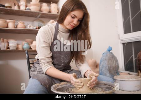 Attractive female potter shaping clay bowl on potters wheel Stock Photo