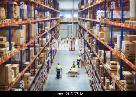 Blur warehouse background. Above view of warehouse workers moving goods and counting stock in aisle between rows of tall shelves full of packed boxes Stock Photo