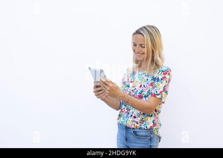 pretty young blonde woman with floral shirt is working with tablet in front of white background Stock Photo