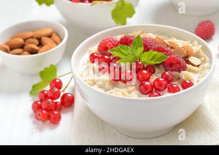 Tasty oatmeal porridge with raspberries, nuts and red currant in bowl on white table Stock Photo