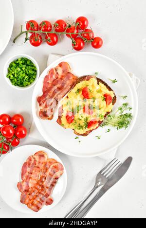 Scrambled eggs with microgreen, bacon and tomato slices on bread. Top view, flat lay Stock Photo