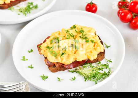 Scrambled eggs with microgreen and bacon on bread, close up Stock Photo
