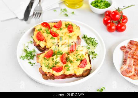 Scrambled eggs with microgreen, bacon and tomato slices on bread, close up Stock Photo