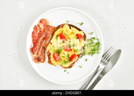 Scrambled eggs with microgreen, bacon and tomato slices on bread. Top view, flat lay Stock Photo