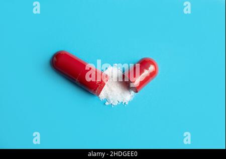 Above view of single red color gel capsule opened, white powder spilled out on light blue background. Pharmaceutical concept. Lot of copy space. Stock Photo