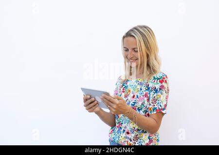pretty young blonde woman with floral shirt is working with tablet in front of white background Stock Photo