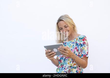 pretty young blonde woman with floral shirt is working with tablet in front of white background Stock Photo
