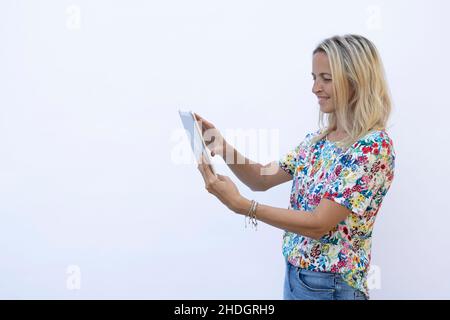 pretty young blonde woman with floral shirt is working with tablet in front of white background Stock Photo