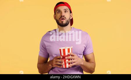 shocked man watching movie and holding popcorn bucket isolated on yellow Stock Photo
