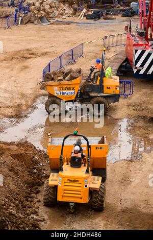 Construction workers & yellow dumper vehicles (1 working & one having a break from work) - York city centre building site, North Yorkshire England UK. Stock Photo