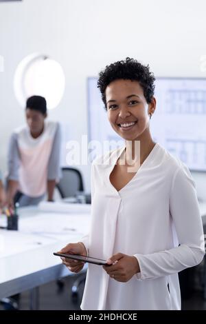 Portrait of smiling businesswoman with tablet pc in conference room while colleague in background Stock Photo