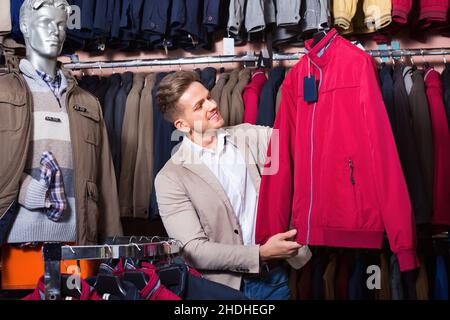 Guy deciding on warm coat in men’s cloths store Stock Photo