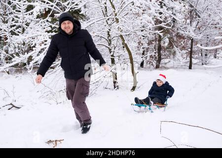 Dad sledding his son at a ski resort in a snow-covered winter forest Stock Photo