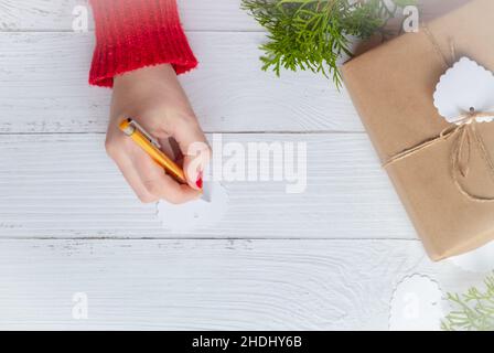 Christmas table with Christmas gift. Woman's hand writing on a gift tag Stock Photo