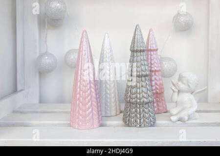 Ceramic figurines of pastel-colored Christmas trees, a white faience angel, a garland of balls made of threads decorate the room before Christmas Stock Photo