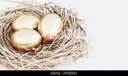 Gold colored eggs in straw nest on white table, copy space Stock Photo