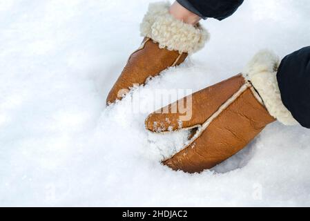 First snow, making snowballs in the park close-up. Hands in warm mittens make snow in winter. Brown leather mittens in the snow in winter. Stock Photo