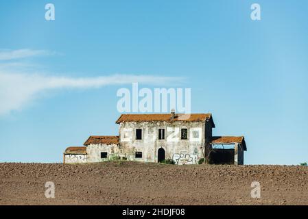 Abandoned house on the hill. Brick building covered with red tiles, broken windows and doors. Around the plowed field Stock Photo