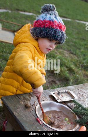 A 3 year old child playing outdoors in a mud kitchen, UK Stock Photo
