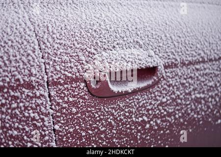 A car door lock is covered with snow and ice while a hand holds a key ...