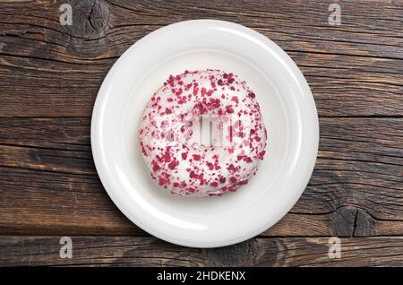 Donut with cream cheese sprinkled of red crumbs in plate on old wooden background, top view Stock Photo