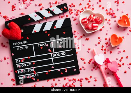 Romantic movie concept. Happy Valentines day. Clapperboard, hearts, sweets, confetti on pink table. Flat lay, top view. Stock Photo