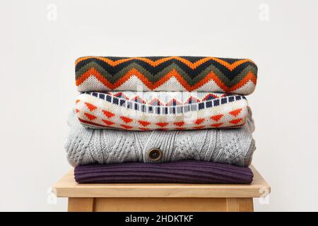 Stack of stylish sweaters on wooden stool against light background Stock Photo