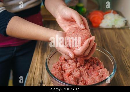 Close-up of a woman's hands preparing ground beef to make hamburgers, the meat is still raw and she is adding the ingredients, nice atmosphere in the Stock Photo