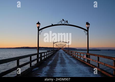 Looking straight down White Rock's wooden pier through the centre of decorative lampposts where pigeons hang out to enjoy blue hour views and sunrise Stock Photo