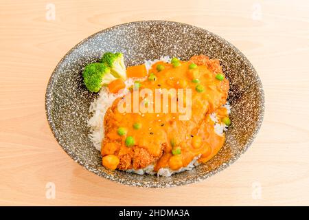 Breaded fried chicken fillet on cooked white rice, green peas and vegetables and lots of red curry Stock Photo