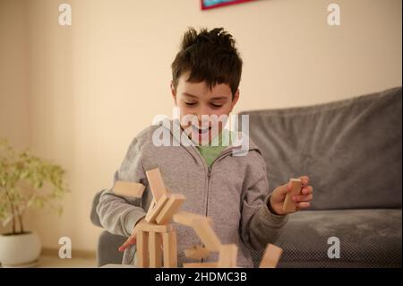 Close-up of a handsome school aged Caucasian boy playing board games and looks surprised when his constructed structure from wooden blocks falling dow Stock Photo