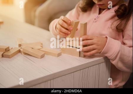 Close-up of little girl hands building wooden structure with blocks and bricks. Fine motor skills development, educational board games concept with co Stock Photo